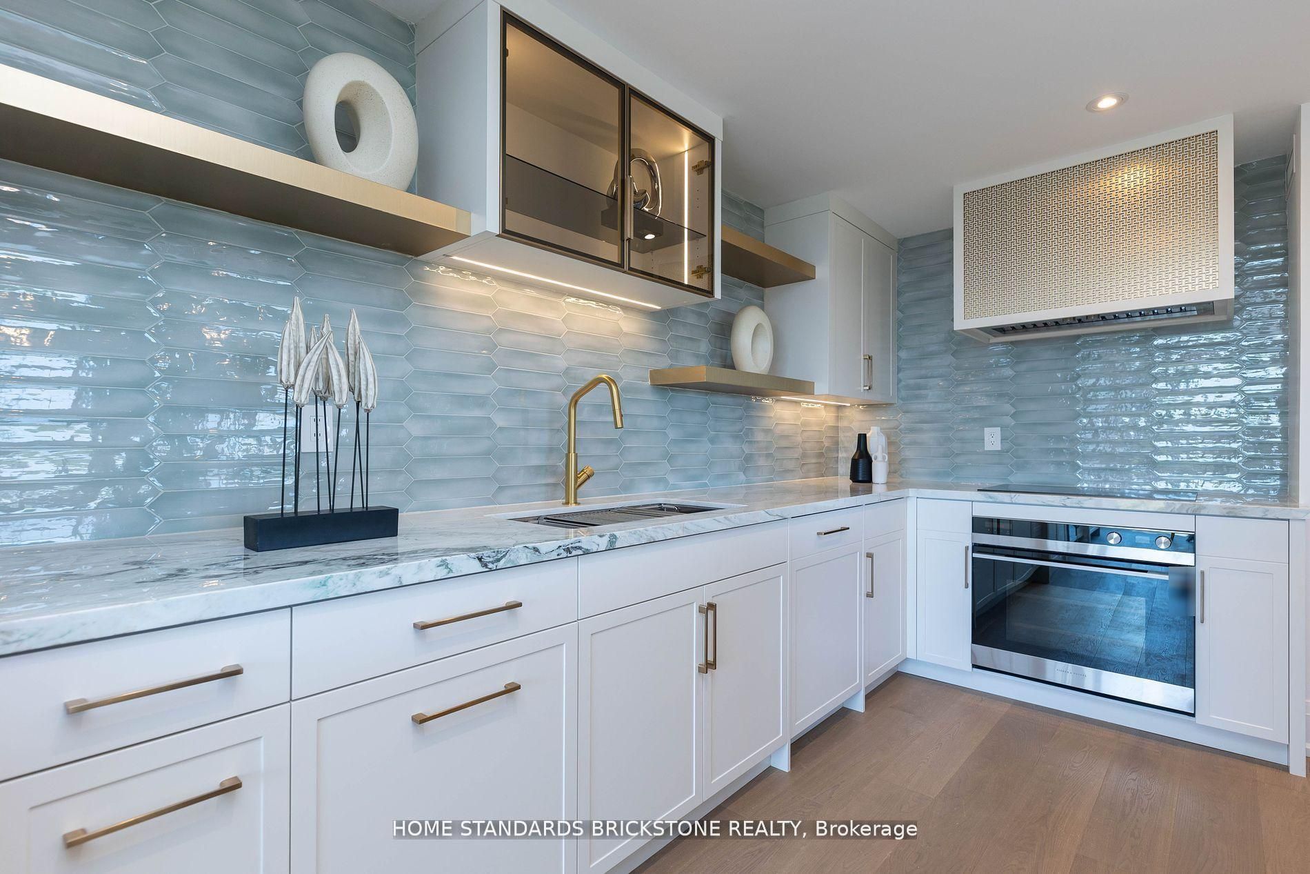 White shaker cabinetry with brass pulls, aqua glass tile backsplash and brass floating shelves
